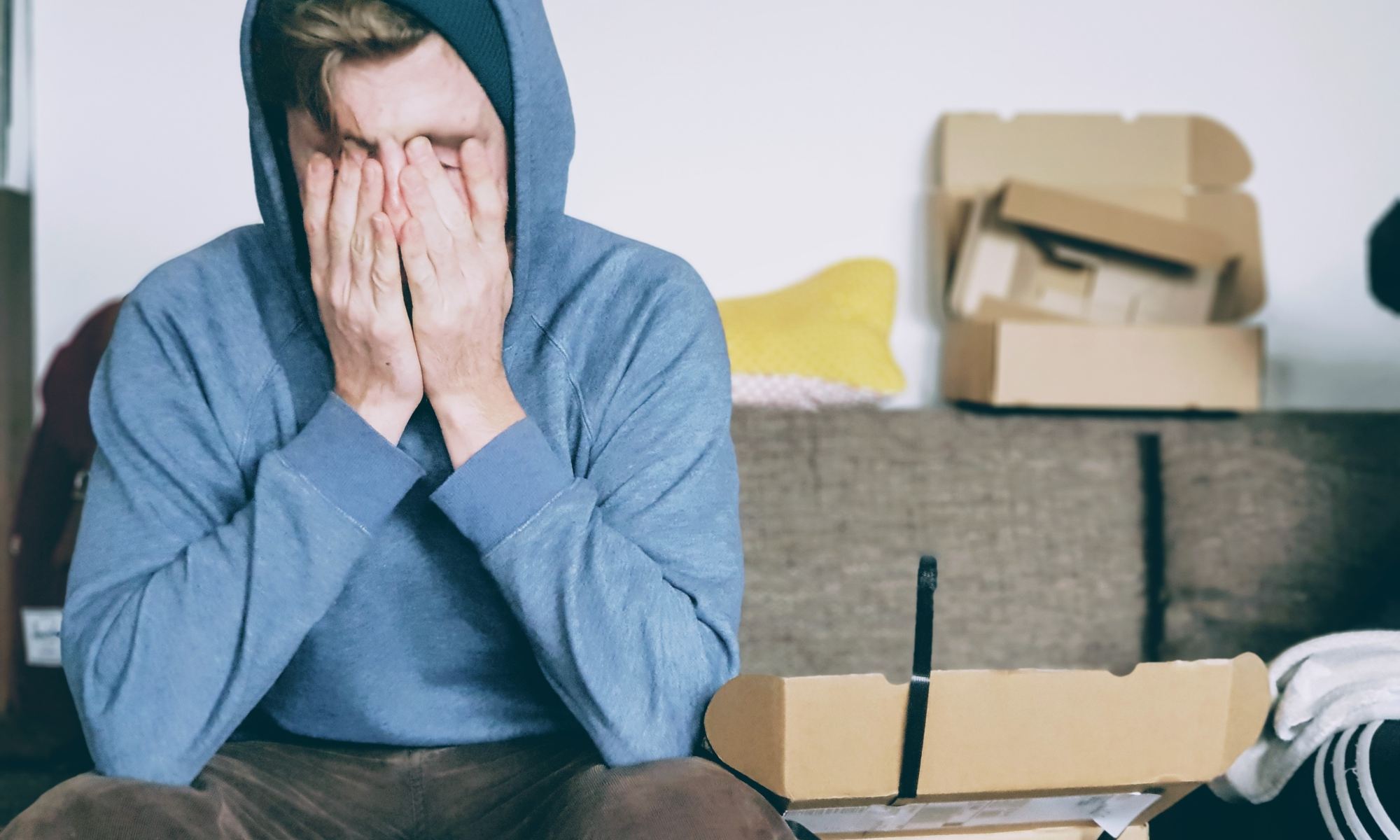 Disappointed young man wearing blue hoodie and covering face with both hands
