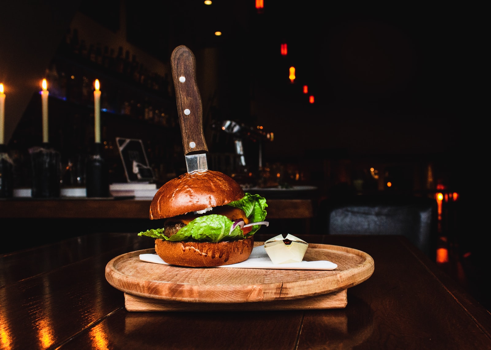 Selective focus photography of big burger with knife into it on brown wooden tray