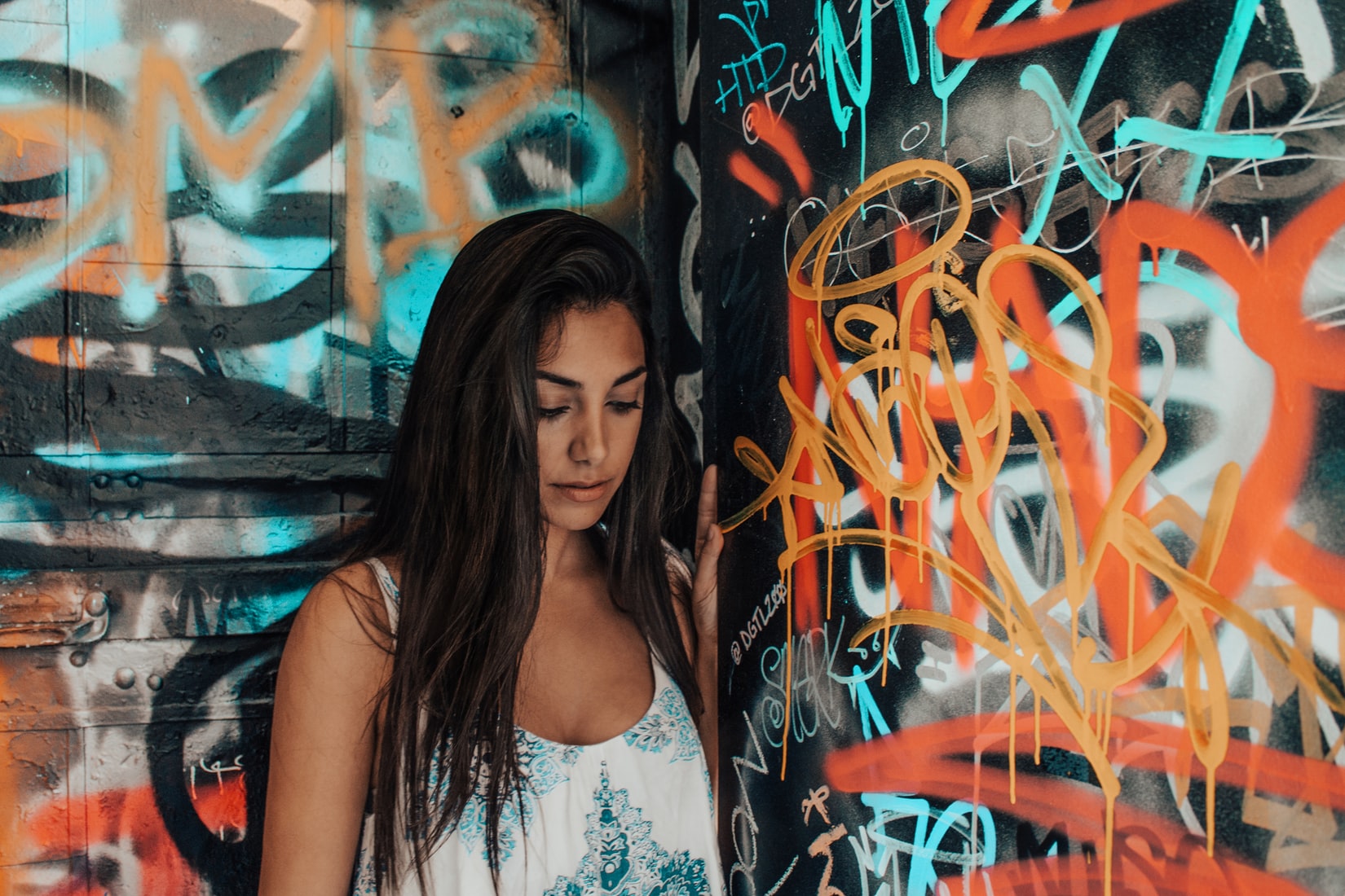 Young brunette woman experiencing negative thoughts while standing next to graffiti wall