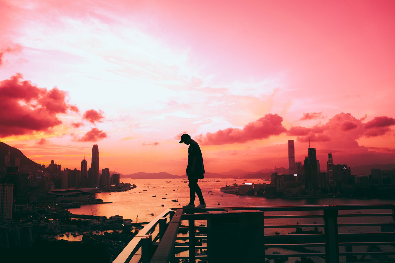 Silhouette of lonely man standing on railing of building in front of body of water and city