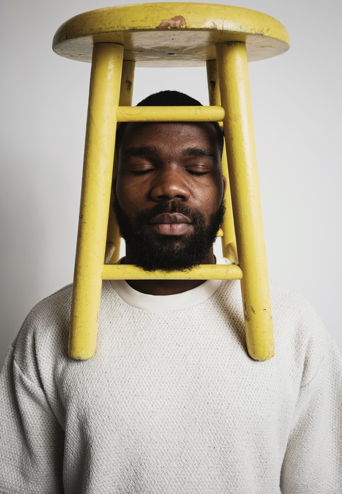 Black man with yellow wooden stool on top of shoulders and head