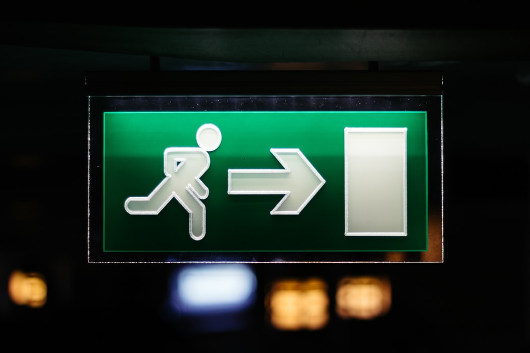 Closeup photo of green and white signage of person running towards arrow and door