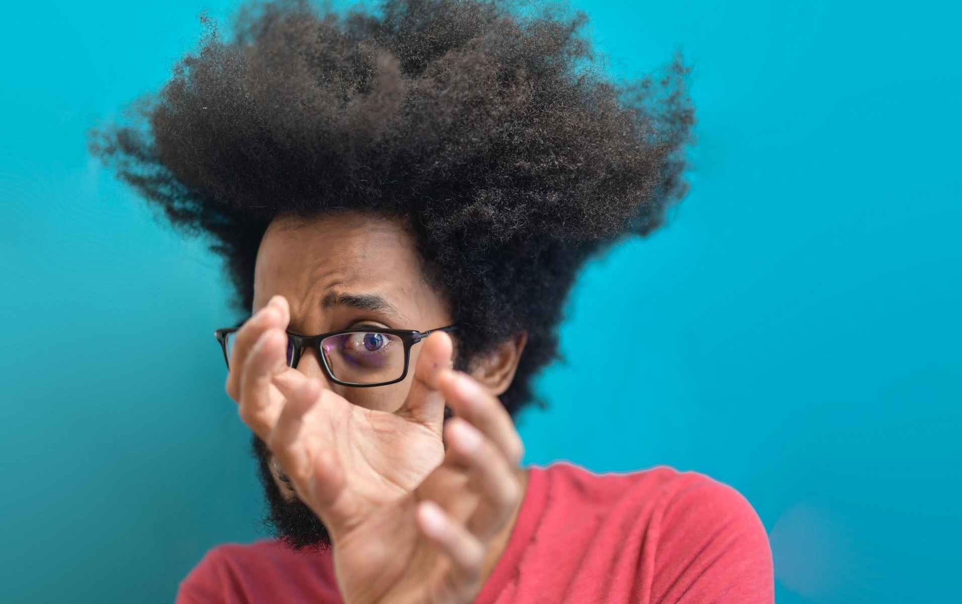 Black man with afro and glasses holding hands in front of left eye