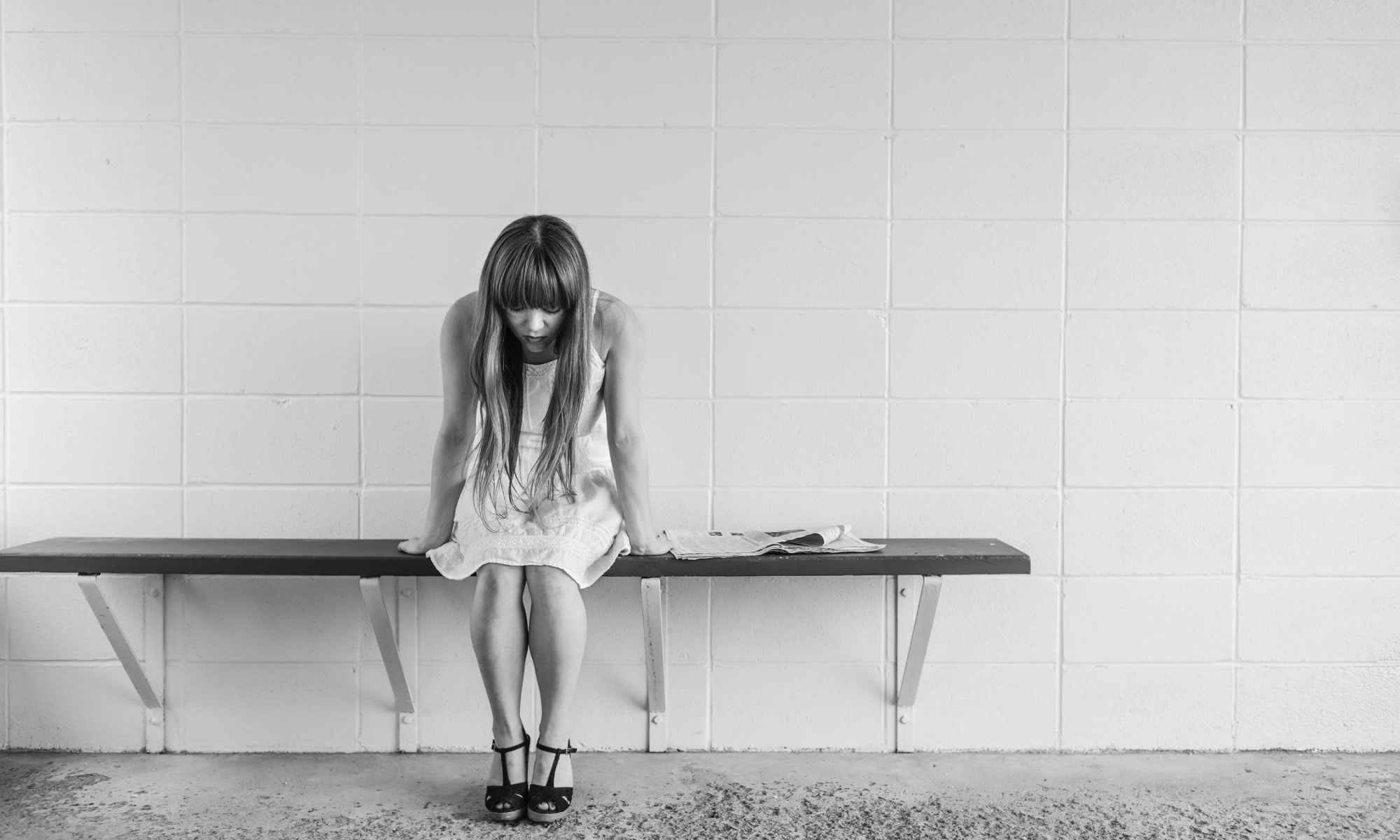 Grayscale photo of depressed woman sitting on bench against wall