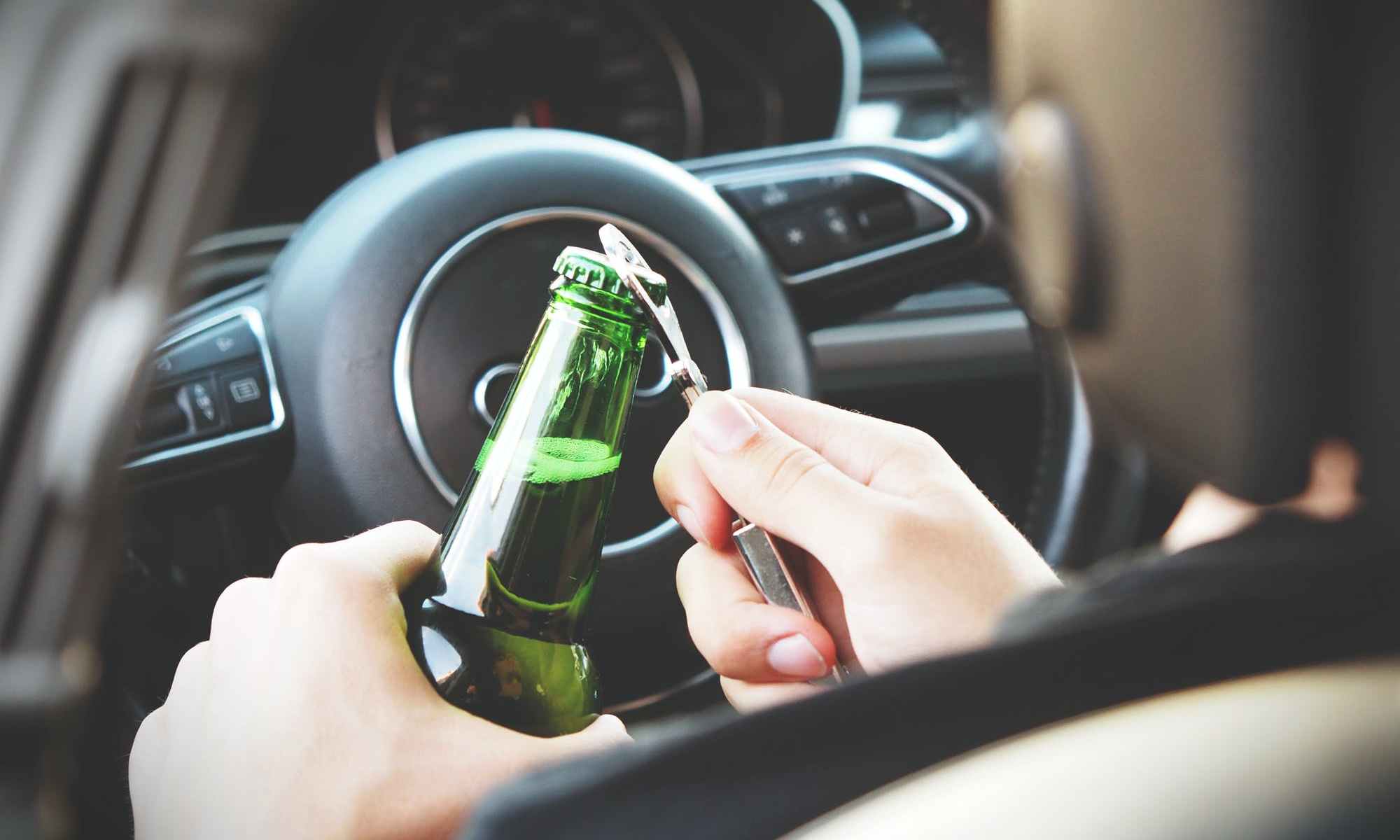 Person opening bottle of beer in car behind wheel