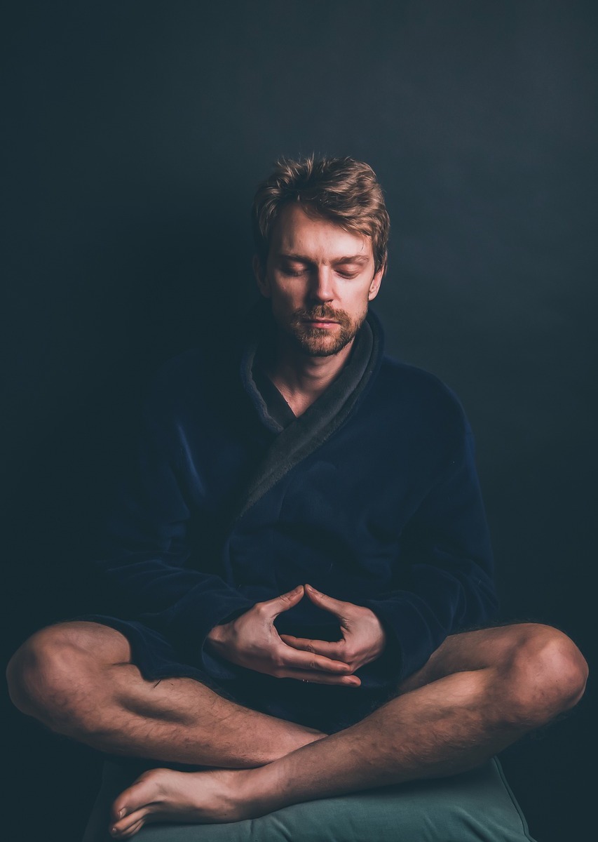 White man sitting on blue pillow meditating